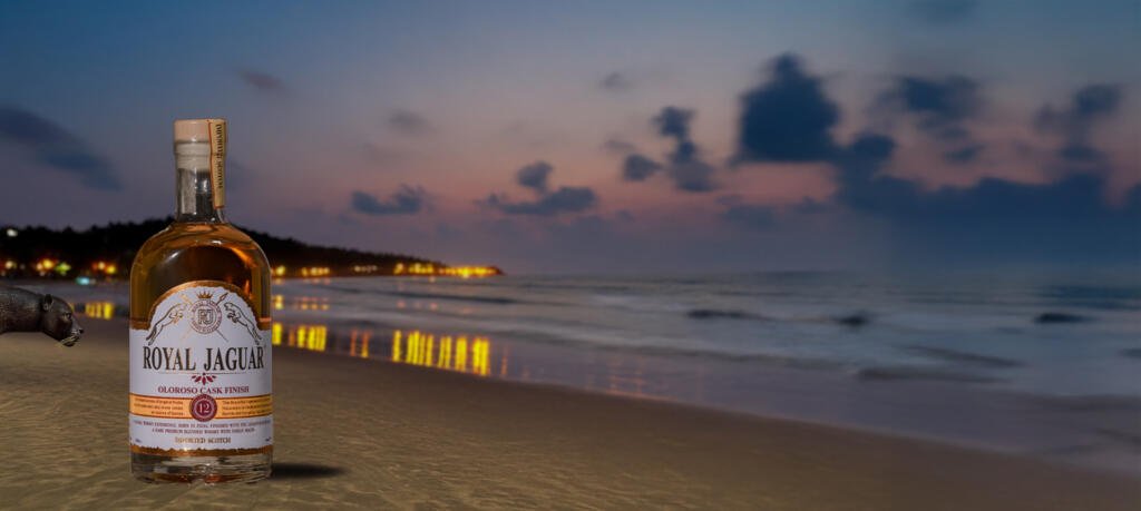 Bottle of Royal Jaguar Imported Scotch with Oloroso Cask Finish placed on a Goa beach at sunset, symbolizing luxury, legacy, and craftsmanship.