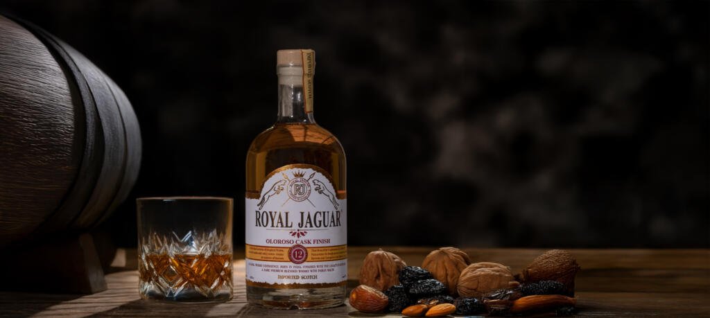 Royal Jaguar Oloroso Cask Finish bottle with whisky glass, wooden cask, and dried fruits symbolizing the rich flavors of sherry cask matured scotch.